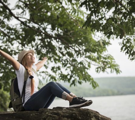 Young happy woman sitting with backpack enjoy the nature after hike. Woman travel concept.