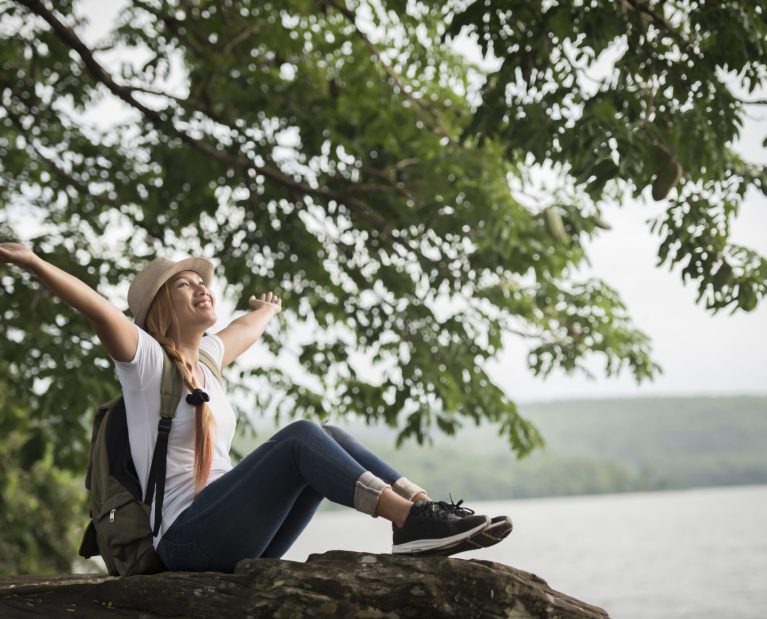 Young happy woman sitting with backpack enjoy the nature after hike. Woman travel concept.